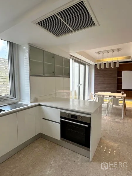 Townhouse for sale in Yan Nawa, Bangkok - Bright white kitchen with peninsula, built-in oven and adjacent dining area with pendant lights
