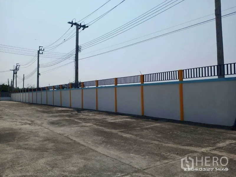 Warehouse for rent in Bang Bo, Samut Prakan - Driveway beside the boundary fence leading toward the gated entrance.