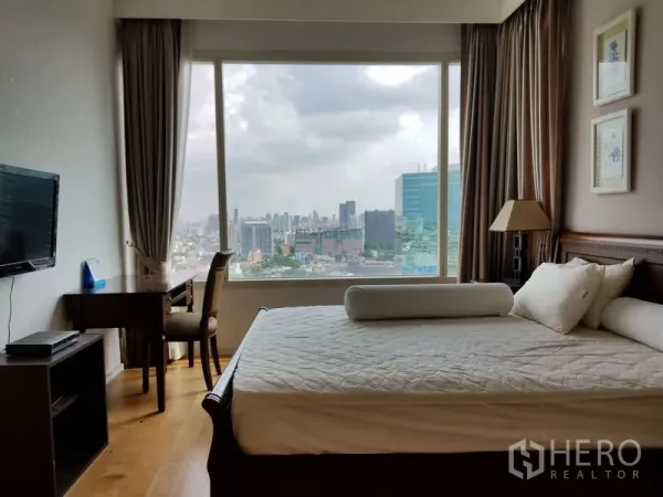 Condominium for rent in Chatuchak, Bangkok - Bedroom with king bed, work desk, wall‑mounted TV and a floor‑to‑ceiling window with city views.
