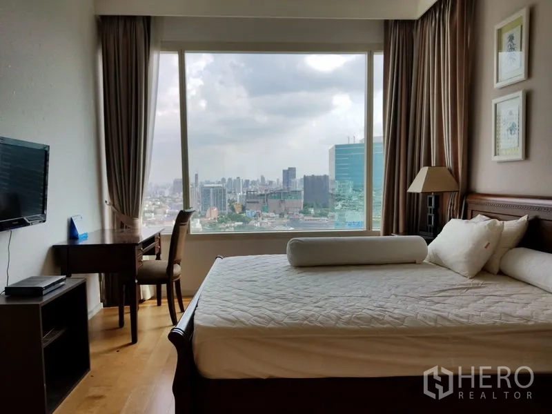 Condominium for rent in Chatuchak, Bangkok - Bedroom with king bed, work desk, wall‑mounted TV and a floor‑to‑ceiling window with city views.