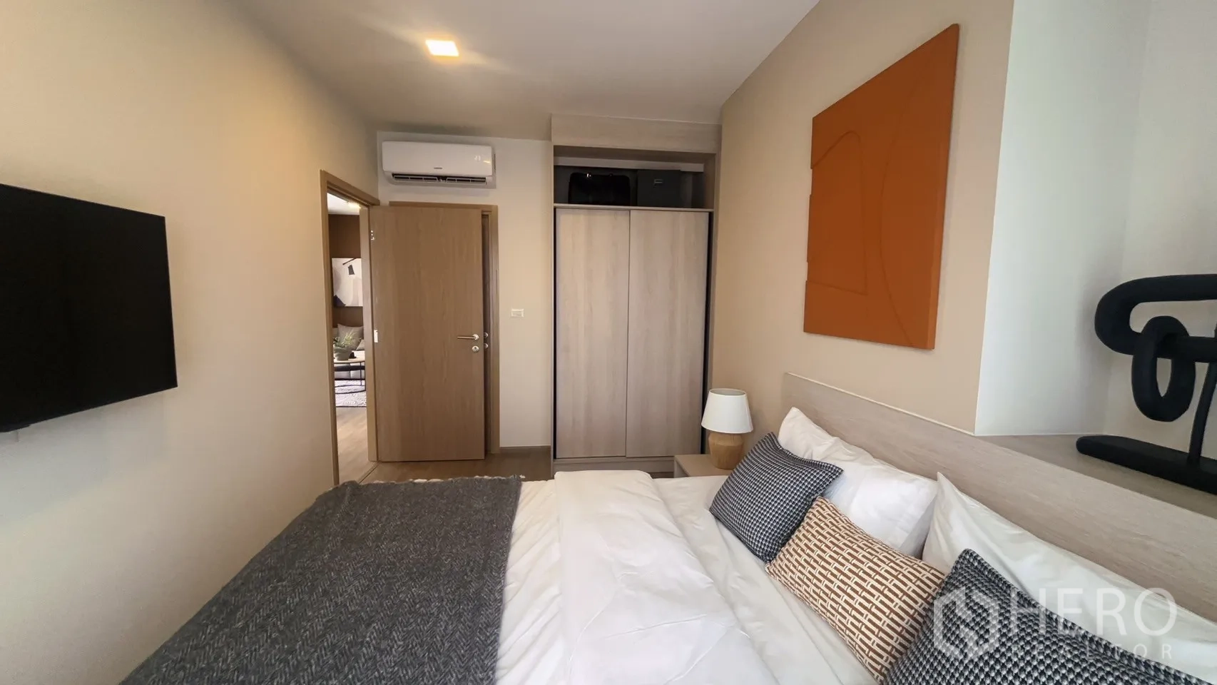 Condominium for rent in Watthana, Bangkok - Bedroom view showing wall-mounted TV, wardrobe with sliding doors, bedside lamp, and air conditioner.