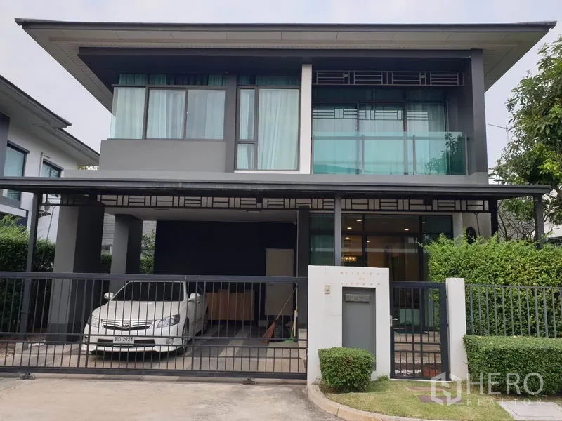 บ้าน ให้เช่าในBang Kapi, Bangkok - ด้านหน้าบ้านเดี่ยวสองชั้นสไตล์โมเดิร์น รั้วรอบพื้นที่ จอดรถมีหลังคา และกระจกบานใหญ่.