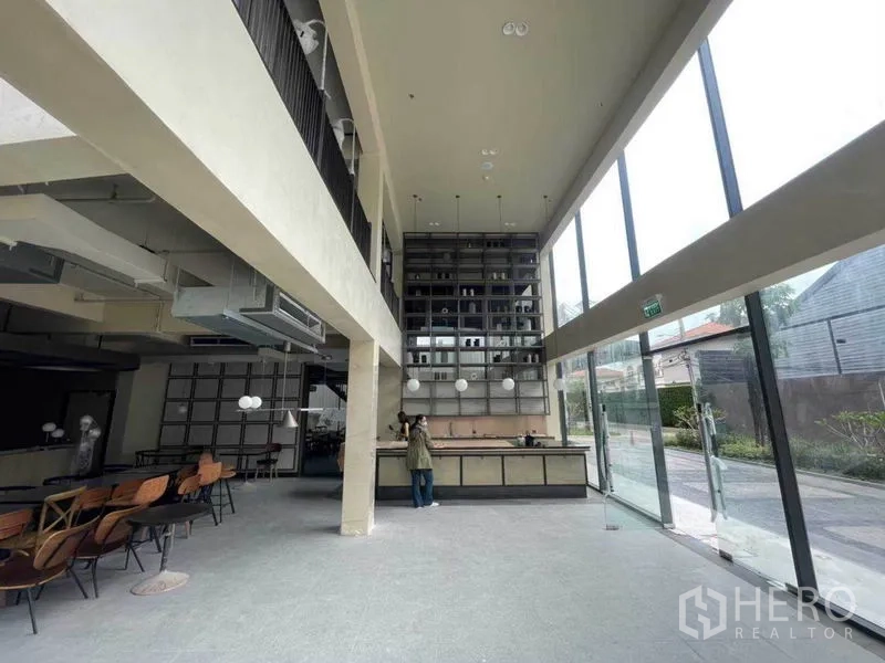 零售空间 出租在Phra Khanong, Bangkok - 挑高零售室内，落地玻璃、服务吧台与高层展示架，位于曼谷帕卡农。