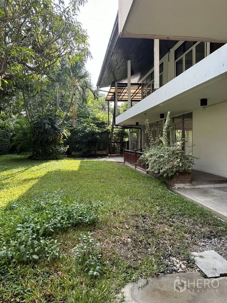 Detached House for rent in Khlong Toei, Bangkok - Shaded side garden with dense trees and shrubs along a white two‑storey house.