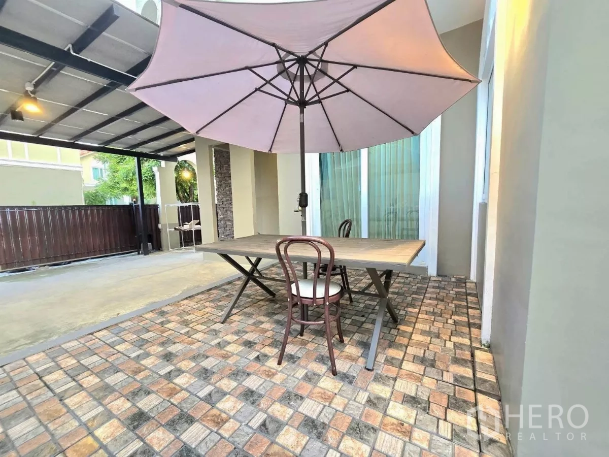 Detached House for rent in Samut Prakan - Outdoor terrace with umbrella dining set next to a covered carport and gate.