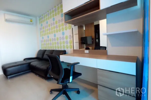 Condominium for rent in Sathon, Bangkok - Modern living room at Rhythm Sathorn-Narathiwas with black leather sectional, built-in desk and shelving, patterned feature wall, and air conditioner.