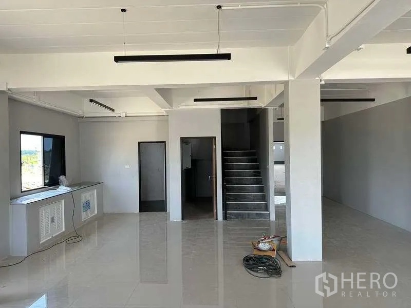 Factory for sale in Khlong Luang, Pathum Thani - Ground-floor office area with tiled floor, staircase, windows and linear LED lighting.