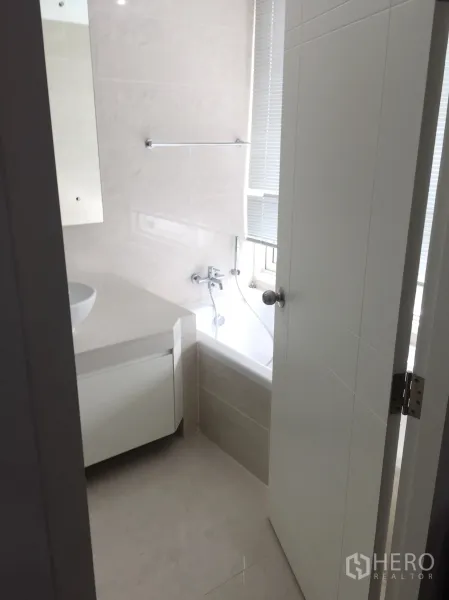 公寓 出租在Khlong Toei, Bangkok - 浅色瓷砖浴室，窗边浴缸与白色洗手柜。