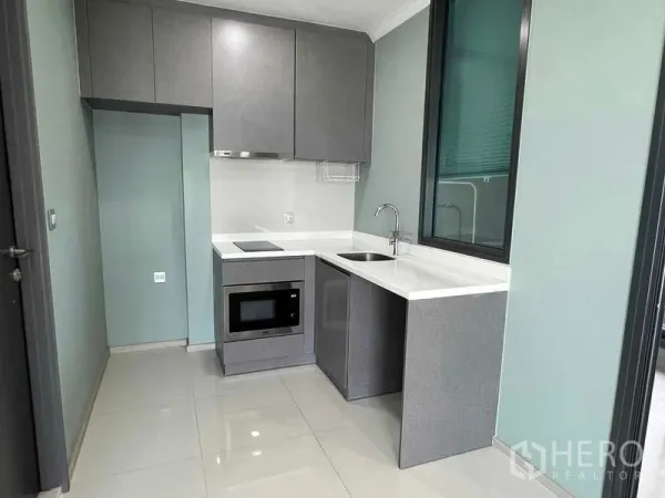 Condominium for sale in Ratchathewi, Bangkok - Compact L-shaped kitchen with built-in cooktop, microwave, sink and ample cabinetry.