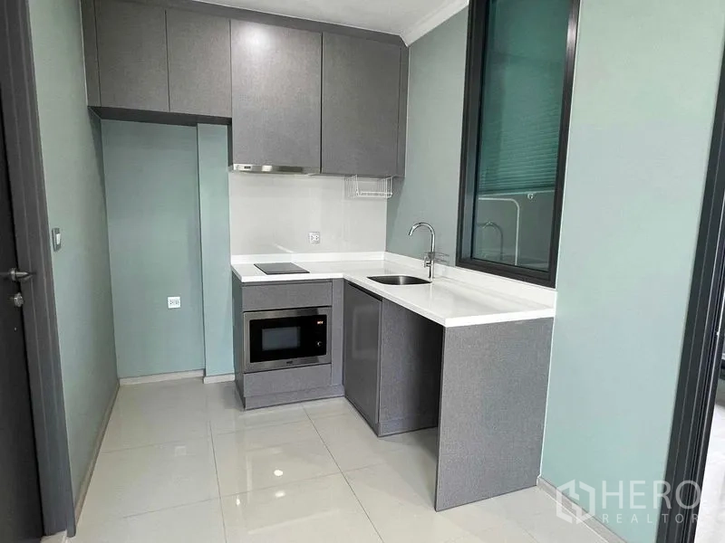Condominium for sale in Ratchathewi, Bangkok - Compact L-shaped kitchen with built-in cooktop, microwave, sink and ample cabinetry.