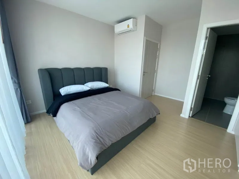 Townhouse for rent in Saphan Sung, Bangkok - Bedroom with upholstered bed, wall-mounted air-conditioner and door to ensuite bathroom.