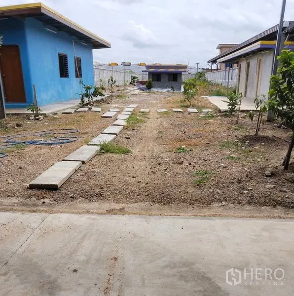 Warehouse for sale in Sai Noi, Nonthaburi - Open yard with stepping-stone path between auxiliary buildings and young trees.