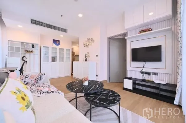 Condominium for rent in Watthana, Bangkok - Open‑plan lounge with sofa, built‑in cabinets and TV console leading toward the kitchen.