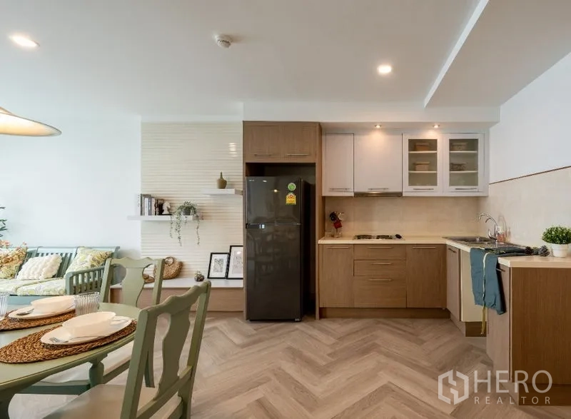 Condominium for sale in Watthana, Bangkok - Modern L-shaped kitchen with upper cabinets, black refrigerator and built-in hob.