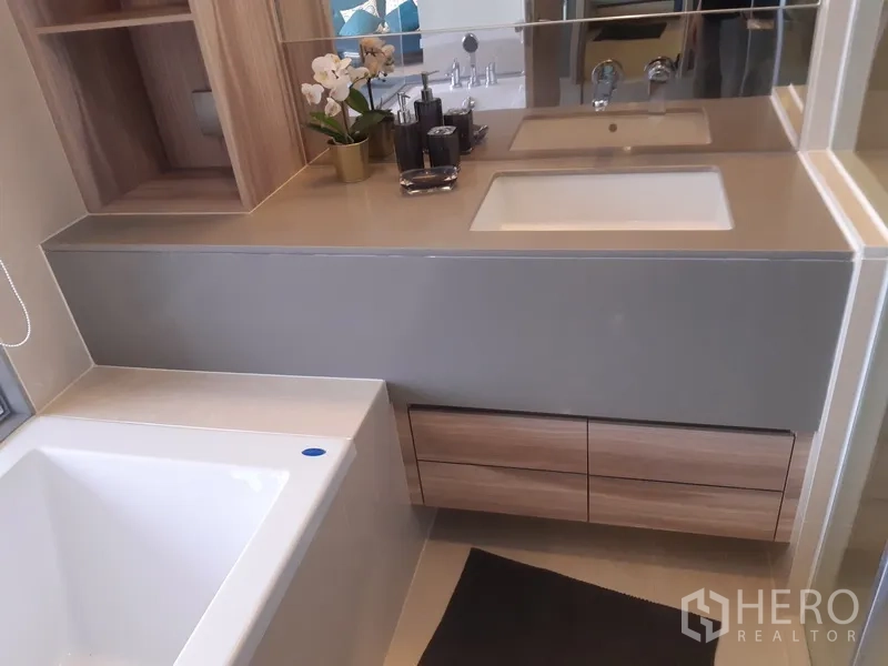 Condominium for rent or sale in Watthana, Bangkok - Vanity area with large mirror, under-sink drawers and bathtub corner with decor.