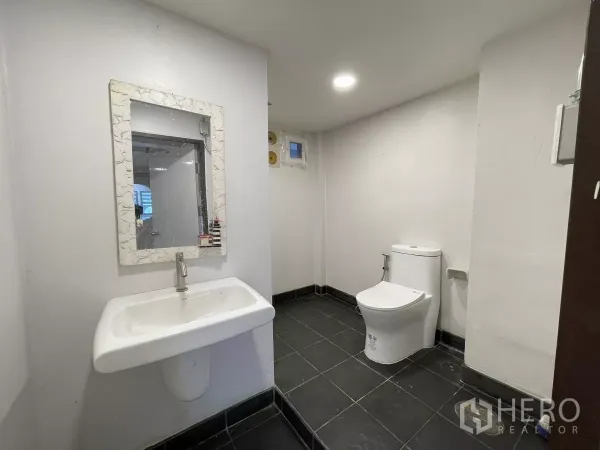 สำนักงานที่บ้าน ให้เช่าในKhlong Toei, Bangkok - ห้องน้ำสะอาดพร้อมอ่างล้างหน้า กระจกกรอบ และโถสุขภัณฑ์บนพื้นกระเบื้องสีเข้ม