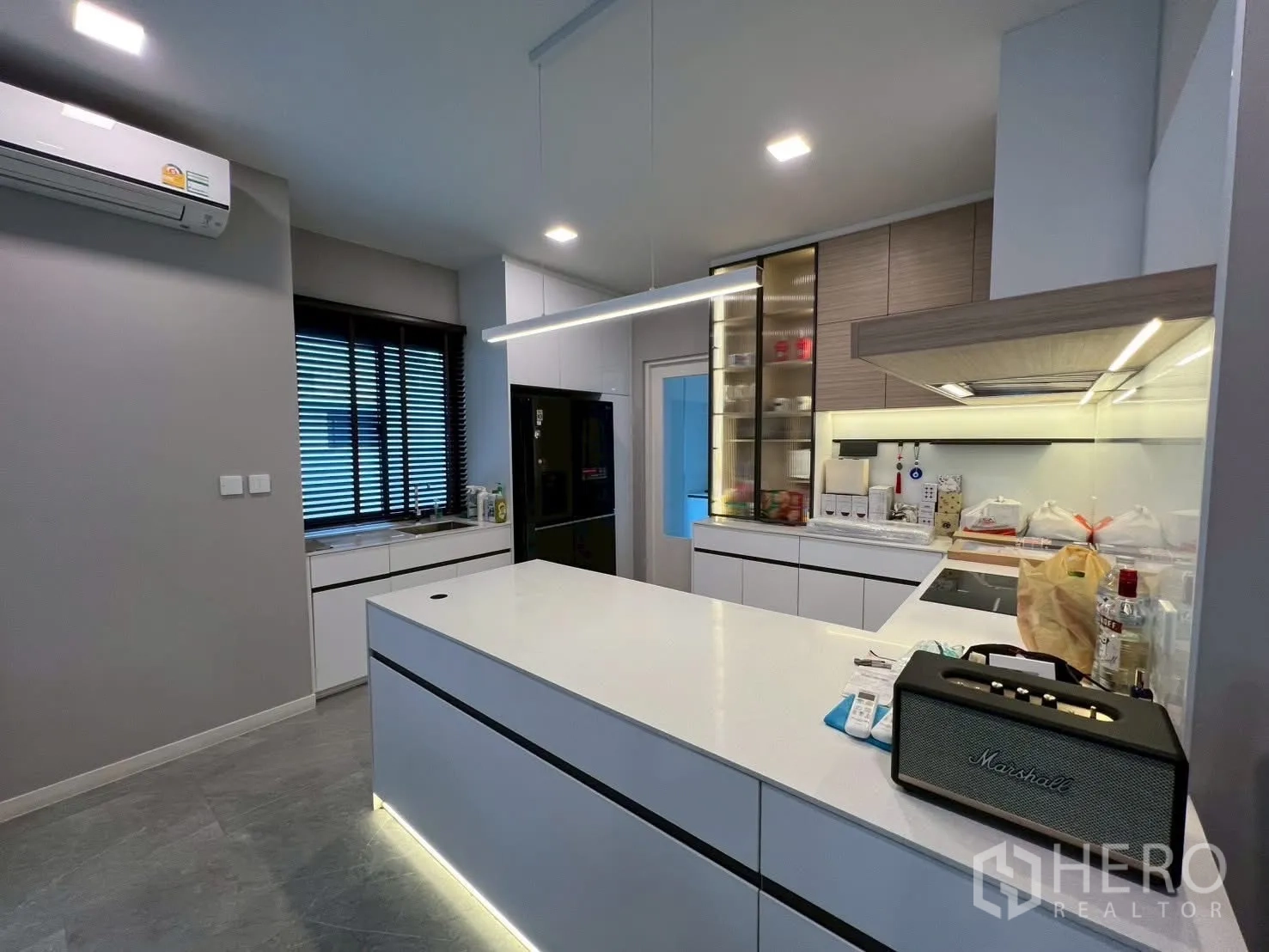 Detached House for rent in Samut Prakan - Sleek Western kitchen with island, hob and hood, under-cabinet lighting, and black fridge.