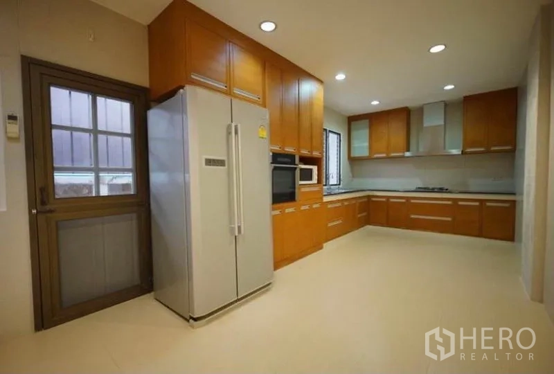 独立式住宅 出租在Bang Phli, Samut Prakan - 现代L形厨房，木质橱柜、嵌入式烤箱与对开门冰箱。