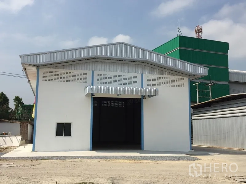 Factory for rent in Pathum Thani - Front exterior of a single‑storey factory with metal roof, canopy and wide entrance over a concrete apron.