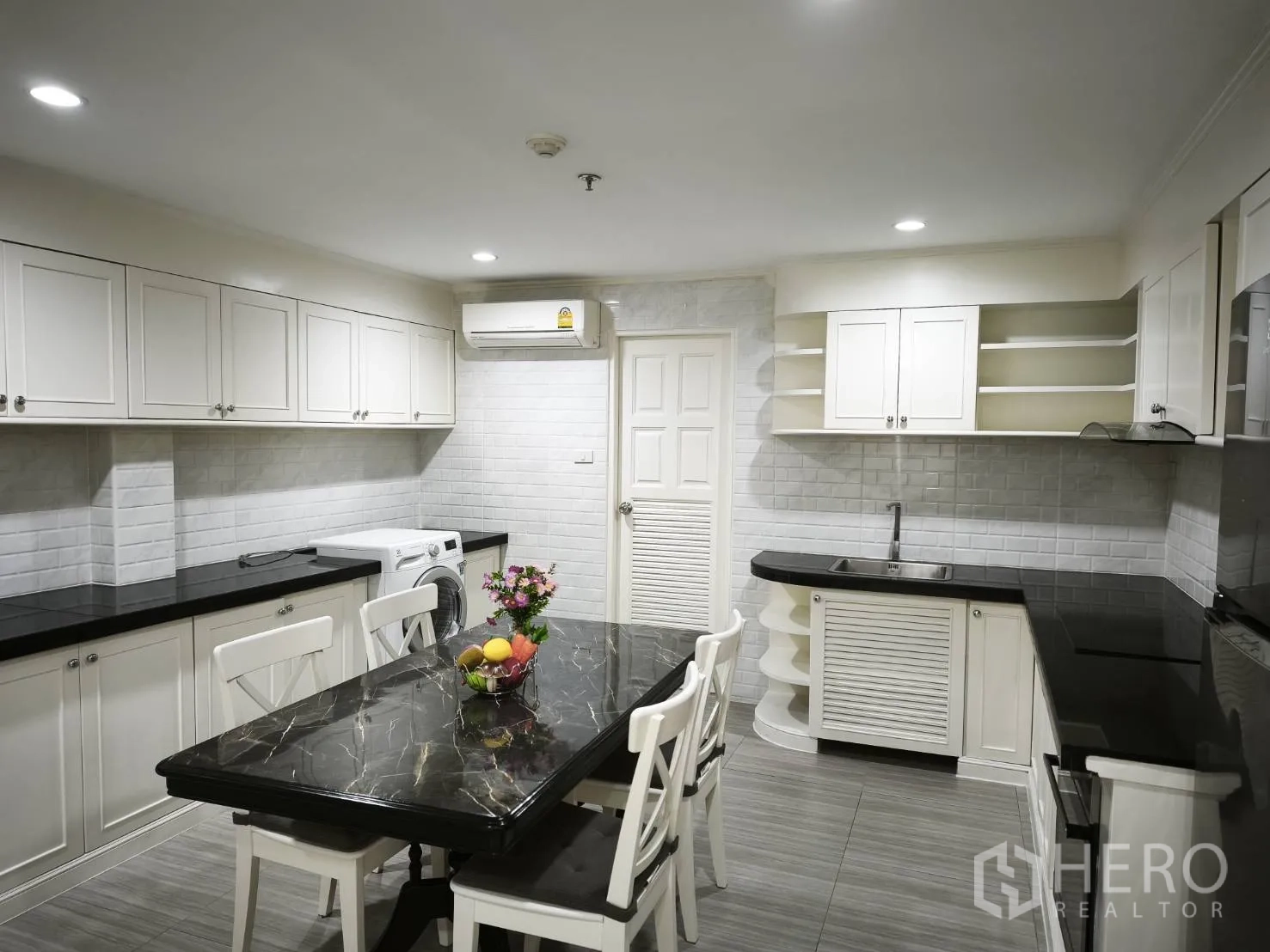 Condominium for rent in Watthana, Bangkok - Spacious white kitchen with black countertops, dining table, and washing machine with ample cabinetry.