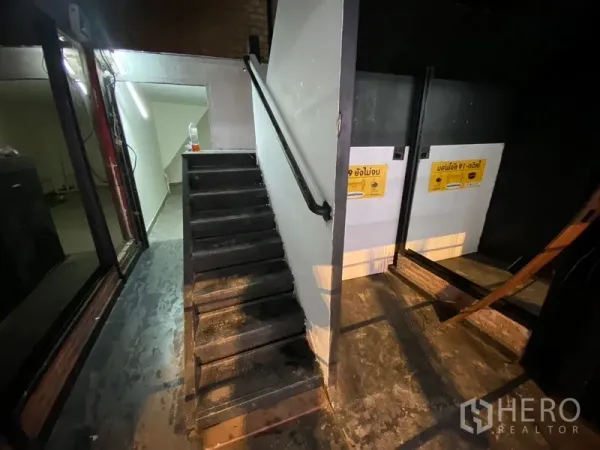อาคารพาณิชย์ ให้เช่าในKhlong Toei, Bangkok - โถงทางเดินสลัวพร้อมบันไดเหล็กสีดำ และทางเข้าห้องน้ำภายในอาคารพาณิชย์.