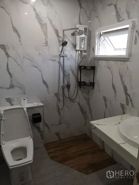 Detached House for rent in Chatuchak, Bangkok - Modern bathroom with marble-look walls, rain shower with electric heater, toilet, and a small window.