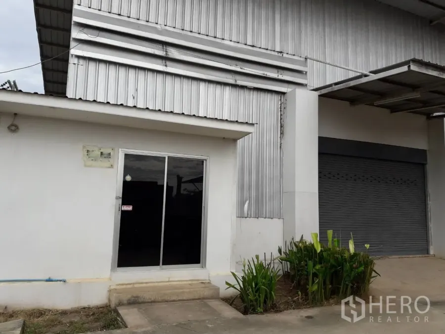 货栈 出租或出售在Khlong Luang, Pathum Thani - 仓库入口，玻璃推拉门、装卸卷闸门与小花坛。