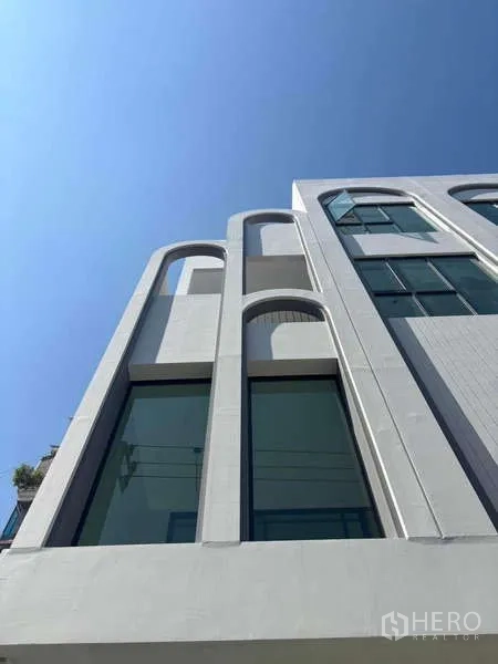 Townhouse for sale - Close-up of white exterior with tall arched window frames against a clear blue sky.