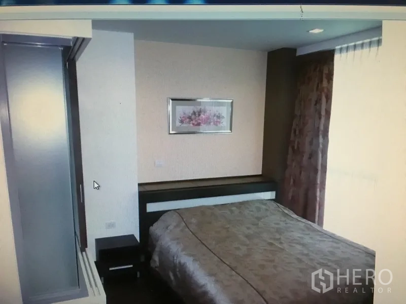 Condominium for rent in Ratchathewi, Bangkok - Cozy bedroom corner with framed artwork, bedside table and soft natural light from tall windows.