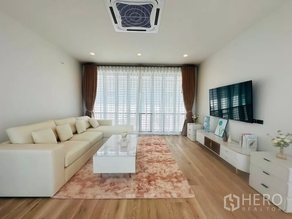 บ้าน ให้เช่าหรือขายในBang Kapi, Bangkok - ห้องนั่งเล่นสว่าง โซฟา L ทีวีผนัง ม่านโปร่ง และพื้นลามิเนตลายไม้