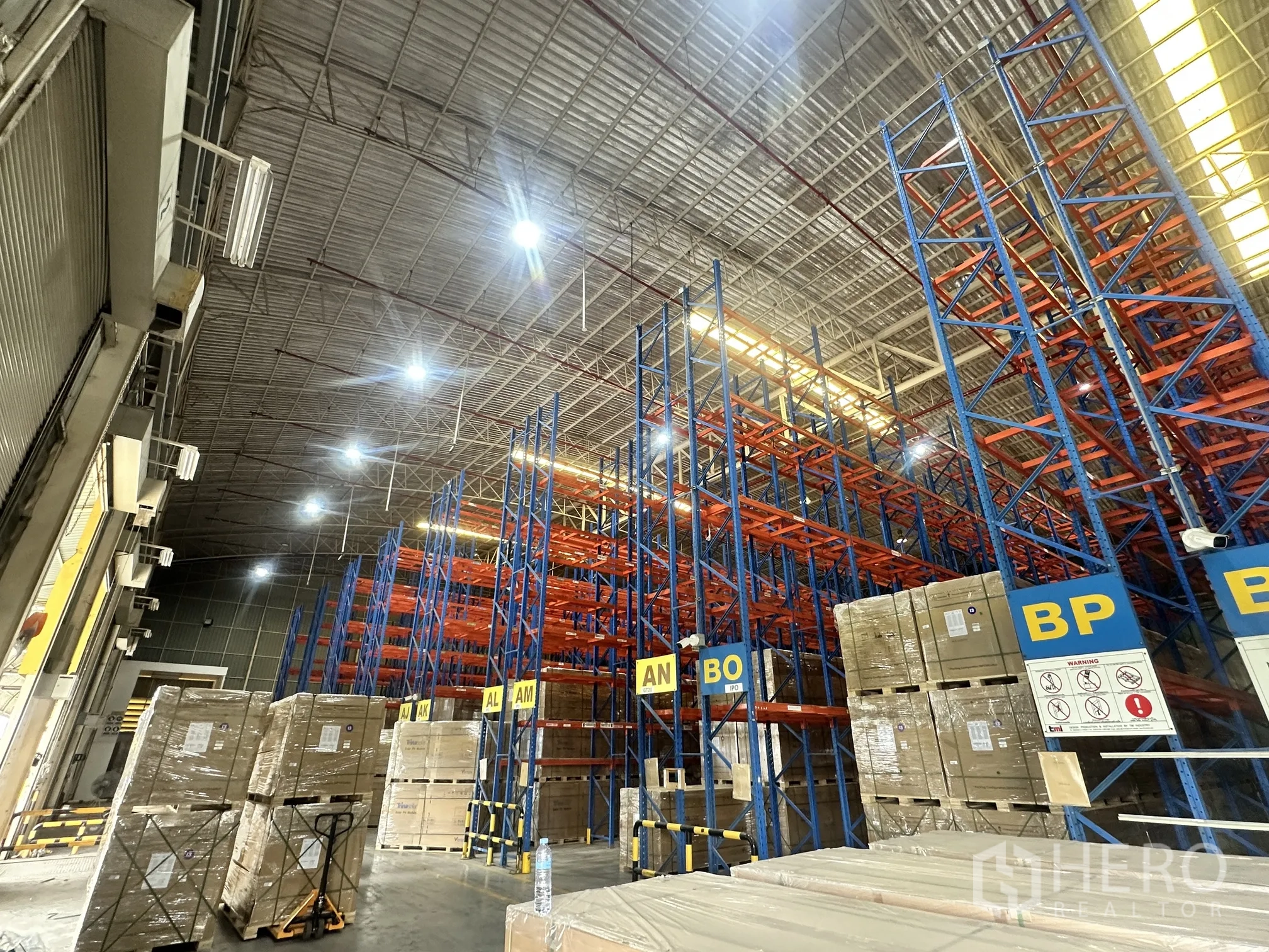 Warehouse for rent in Lat Krabang, Bangkok - Interior view showing racking, pallet stacks, and overhead lighting near loading area.