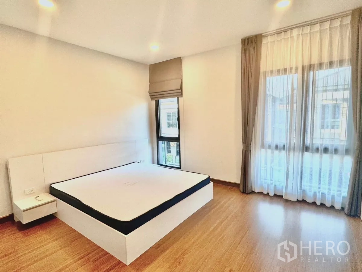 Detached House for rent in Bang Phli, Samut Prakan - Bright bedroom with white platform bed, corner windows and layered drapes.