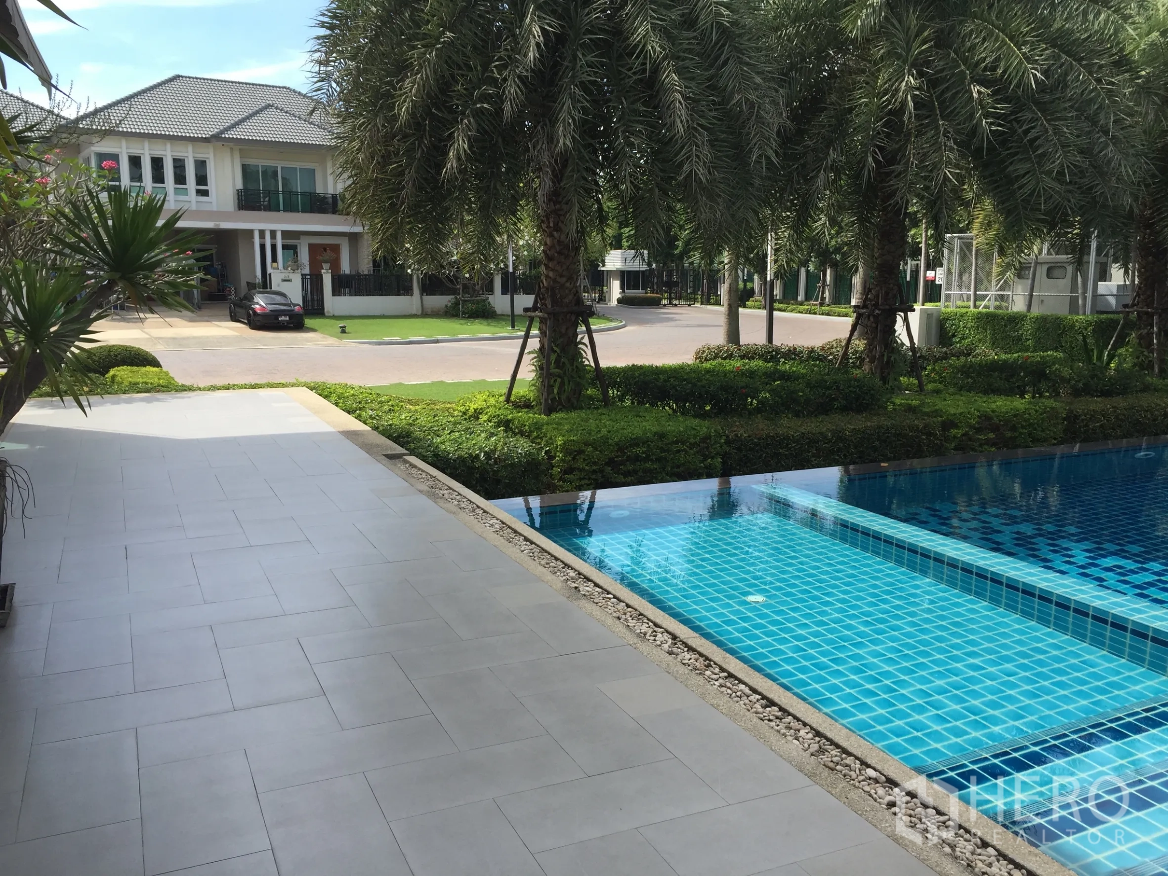 Detached House for sale in Saphan Sung, Bangkok - Gated estate facilities with a blue-tiled swimming pool and palm-lined landscaping.