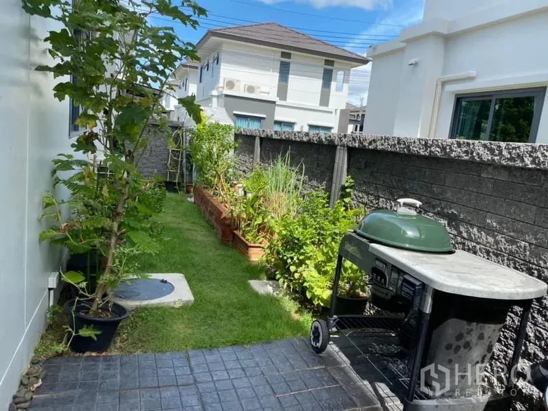 Detached House for rent in Bang Phli, Samut Prakan - Side garden with lawn, planter boxes and a portable barbecue along a paved walkway.