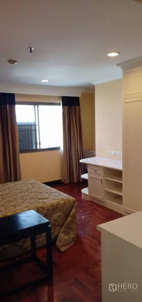 คอนโด ให้เช่าในWatthana, Bangkok - มุมห้องนอนมีโต๊ะทำงานและชั้นเก็บของบิลท์อิน หน้าต่างบานใหญ่ พื้นปาเกต์ และไฟฝ้าเพดานนุ่มนวล