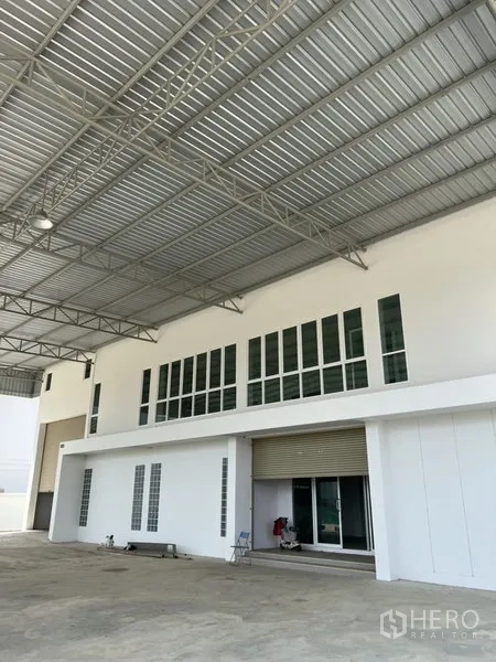 Factory for rent or sale in Bang Bo, Samut Prakan - Ground-floor loading bay with roller shutter and upper-floor office windows beneath a steel canopy.