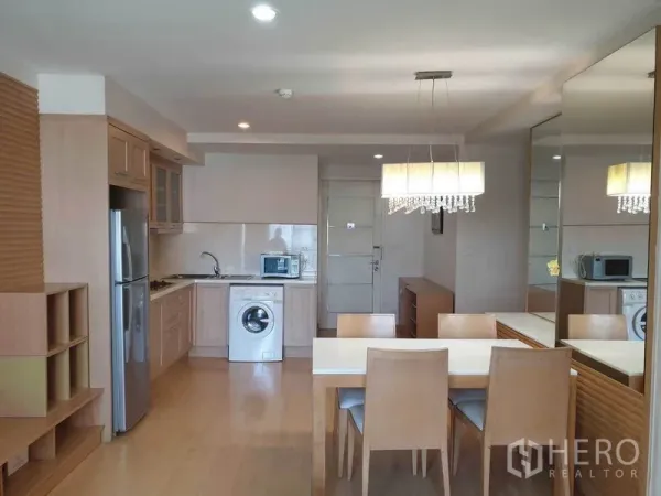 Condominium for rent in Watthana, Bangkok - Open-plan living and dining area with chandelier, mirror wall, and built-in kitchen with washing machine and stainless refrigerator in a Bangkok condo.