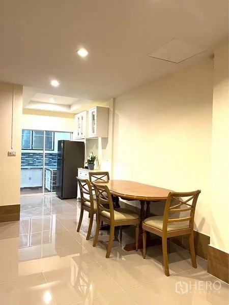 联排别墅 出租在Bang Na, Bangkok - 餐区设圆形木桌和椅子，旁边连接厨房与冰箱。