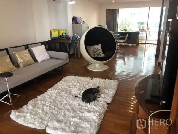 Condominium for sale - Spacious living room with wooden floors, white shag rug, modern pod chair and balcony access.