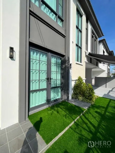 Detached House for rent or sale in Samut Prakan - Front elevation of detached house with gated driveway and landscaped lawn.