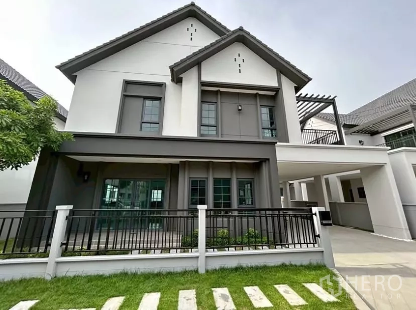 独立式住宅 出租在Bang Phli, Samut Prakan - 现代两层独栋别墅，灰白外立面与人字屋顶，前庭草坪与围栏。