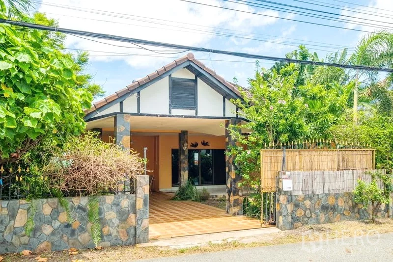 Detached House for sale in Bang Lamung, Chon Buri - Front exterior of a single-storey detached house with stone fence, covered carport, and lush tropical greenery.