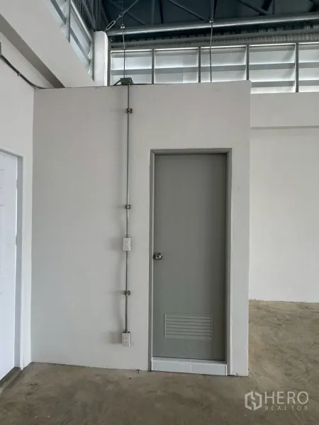 Warehouse for rent or sale in Nong Chok, Bangkok - Interior corner of warehouse showing white utility room with door and exposed electrical conduit.