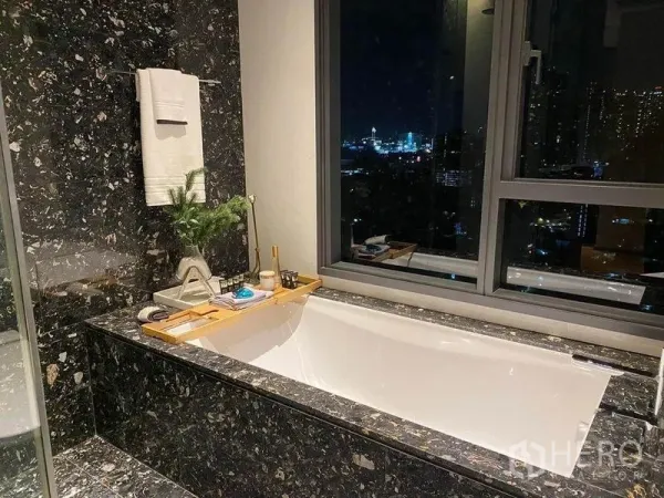 Condominium for rent or sale in Khlong Toei, Bangkok - Marble-clad bathroom with a soaking tub facing a night skyline through a large window.
