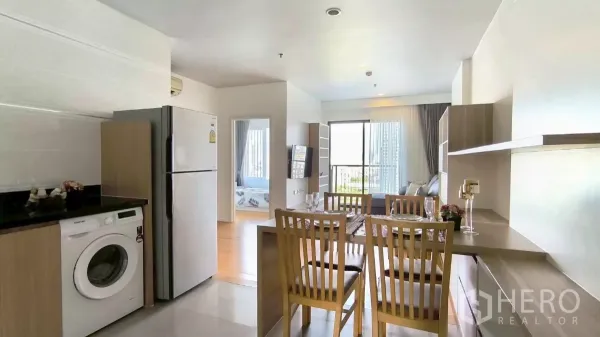 Condominium for rent in Watthana, Bangkok - Kitchen-dining zone with refrigerator, washing machine, and dining set facing the balcony.