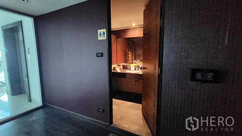 店屋 出租在Khlong Toei, Bangkok - 商铺内带有洗手台与指示标志的卫生间入口。