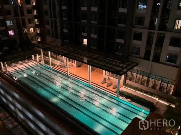 คอนโด ให้เช่าหรือขายในRatchathewi, Bangkok - วิวสระว่ายน้ำแบบสระยาวของคอนโดตอนกลางคืน พร้อมชานพักผ่อนและเตียงอาบแดด