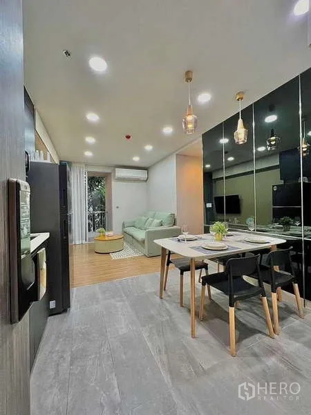 Condominium for sale in Watthana, Bangkok - Open-plan dining and kitchen beside the living area with pendant lights and mirrored wall.