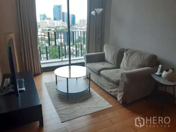 公寓 出租在Khlong Toei, Bangkok - 明亮客厅，配沙发与圆形茶几、电视柜，带阳台可眺望曼谷天际线。