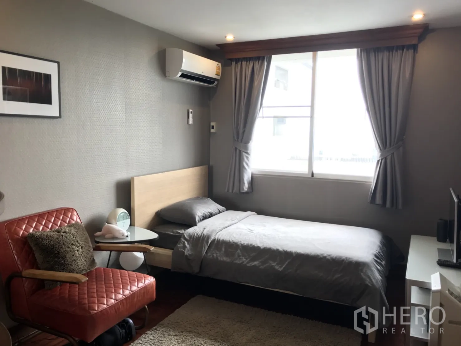 Condominium for rent in Watthana, Bangkok - Guest bedroom with single bed, large window, gray curtains and red accent chair.